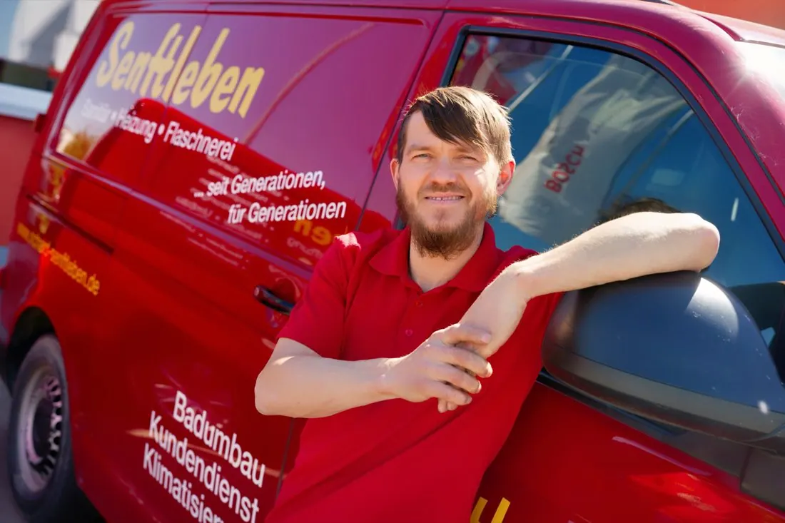 Benjamin Senftleben lehnt am roten Firmenwagen von Senftleben Haustechnik